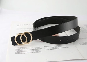 Détail d'une ceinture en cuir noir avec boucle double anneau dorée sur magazine