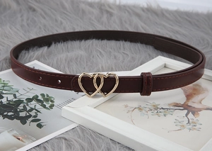 Close-up of thin brown leather belt with a golden double heart buckle on soft plush surface