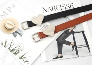 Flat lay of black and brown heart buckle belts over fashion magazines backdrop