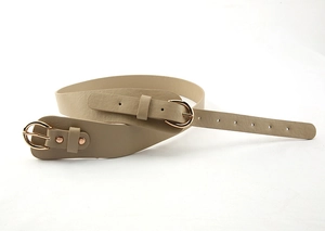 Détail d'une ceinture en cuir kaki avec deux boucles dorées en D sur tissu blanc épuré
