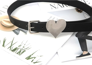 Detailed view of black leather belt with large silver heart buckle on a magazine background