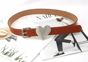 Detail of a dark brown leather belt with a large silver heart-shaped buckle on a magazine