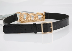 Détail d'une ceinture noire croco avec chaîne dorée audacieuse et boucle carrée chic