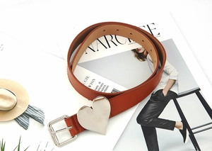 Macro detail of brown leather belt featuring a large silver heart ornament and pin buckle