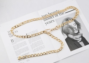Close-up of golden chain belt with flat oval links and metal hook clasp on magazine