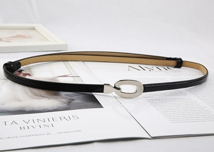 Détail d'une fine ceinture en cuir verni noir avec boucle argentée sur magazine