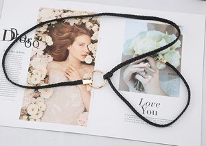 Détail d'une fine ceinture tressée noire avec boucle dorée ronde sur un magazine