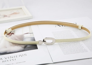Détail d'une ceinture fine crème avec boucle ovale argentée posée sur un magazine