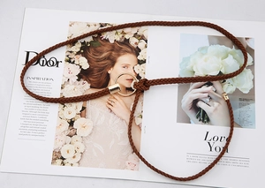 Détail d'une fine ceinture tressée marron avec une boucle ronde dorée sur un magazine