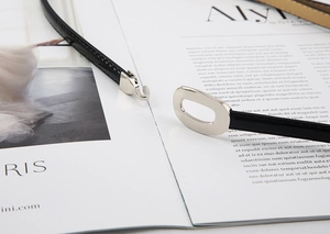 Détail de ceinture fine en cuir noir avec boucle ovale argentée sur un magazine