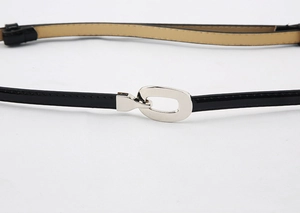 Detail de la ceinture fine en cuir verni noir avec une boucle ovale argentee sur fond blanc