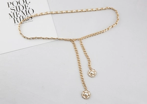 Detail einer goldenen Metallkette mit weißem Leder und floralen Perlenanhängern