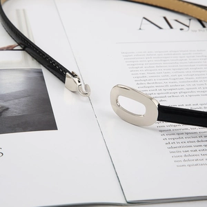 Fine ceinture noire minimaliste avec boucle crochet argentée sur un magazine blanc