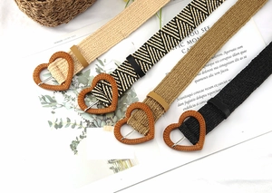 Detail of four woven straw belts in beige, khaki, and black with heart-shaped wooden buckles