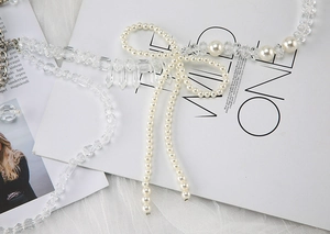 Close-up of pearl beaded strap with crystal bowknot and tassel detail on white fabric