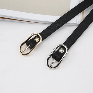 Dettaglio di cinture sottili in pelle nera con fibbie ovali in oro e argento su sfondo bianco