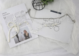 Detail of beaded vest accessory featuring white pearls and a woven bow on mesh fabric