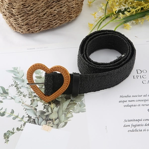 Women's black woven straw belt with a natural wood-textured heart buckle on a magazine