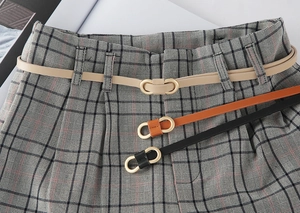 Close-up of slim faux leather belts in apricot, brown, and black with gold buckles
