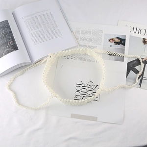Detail of elegant white woven pearl waist chain on a minimalist white fabric background