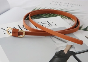 Brown leather waist belt with gold oval buckle placed on a fashion magazine