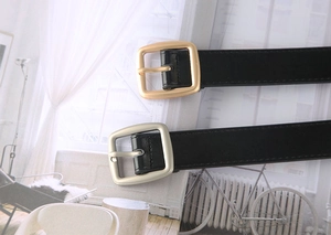 Detail of minimalist black leather belts with matte gold and silver square metal buckles