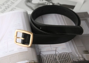 Detailed view of black leather belt with golden square metal buckle and fine stitching