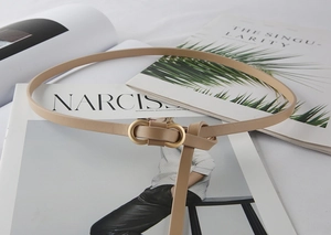 Detail of slim beige leather belt for women featuring a matte gold oval double ring buckle