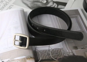 Detailed macro view of the black leather belt featuring a matte silver square pin buckle