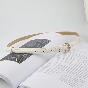 Detail view of slim white belt with gold round buckle on open magazine page