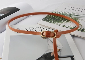 Detail of slim caramel leather belt with matte gold buckle on fashion magazines