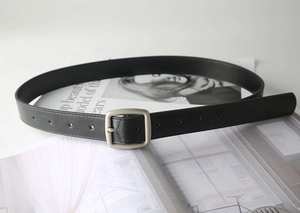 Close-up of black leather belt with silver brushed buckle on a fashion magazine