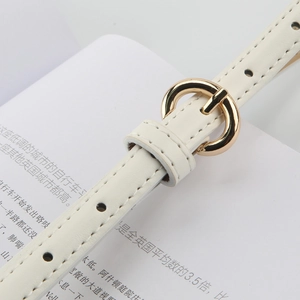Close-up of a slim cream leather belt featuring a round gold buckle and fine stitching