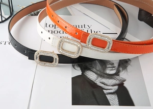 Close-up of three skinny belts in black, white, and orange with rhinestone buckles