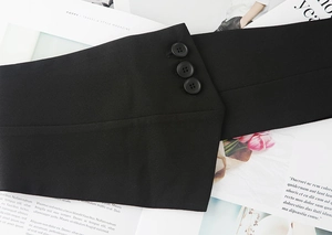 Dettaglio di cintura a corsetto in tessuto nero con chiusura a tre bottoni su rivista