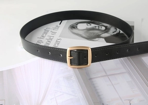Detailed shot of a black matte leather belt with a golden square buckle on a magazine
