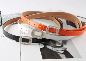 Detail of slim patent leather belts with rhinestone buckles in orange, white, and black