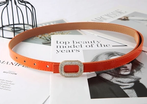 Close-up of orange patent leather skinny belt with sparkling rhinestone buckle detail