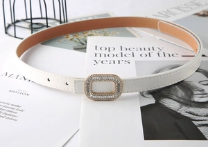 Detail of white leather belt with a rectangular rhinestone buckle on a fashion magazine