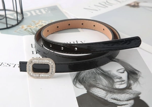 Detail of skinny black patent leather belt featuring a crystal-encrusted rectangular buckle