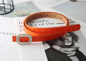 Close-up of bright orange skinny patent leather belt with sparkling rhinestone buckle