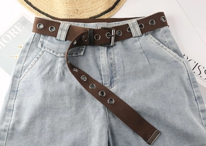 Detail eines braunen Stoffgürtels mit zweireihigen Metallösen auf hellblauen Jeans