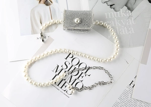 Détail d'un mini sac en strass avec fermoir perle et bandoulière chaîne sur magazines
