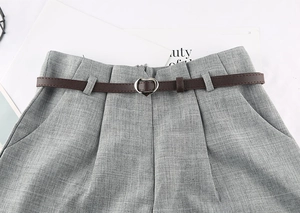 Dettaglio di sottile cintura marrone con fibbia a cuore su pantaloni sartoriali grigi