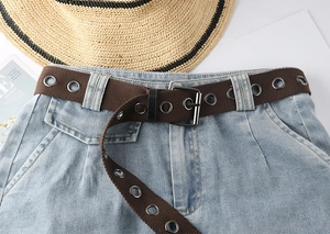Nahaufnahme brauner Canvas-Gürtel mit Metallösen und Dornschließe auf hellblauer Jeans