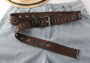 Detail eines braunen Stoffgürtels mit silbernen Doppelösen auf einer hellblauen Jeans