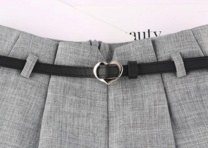 Dettaglio di sottile cintura nera con fibbia a cuore argentata su pantaloni grigi