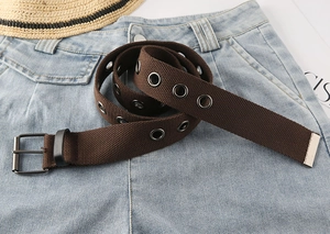 Nahaufnahme von braunem Segeltuchgürtel mit Metallösen und Schnalle auf blauer Jeans