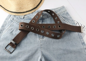 Detailansicht eines braunen Leinwandgürtels mit Metallösen und Silberschnalle auf Jeans