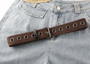 Detail eines dunkelbraunen Leinengürtels mit silbernen Metallösen auf Jeansstoff